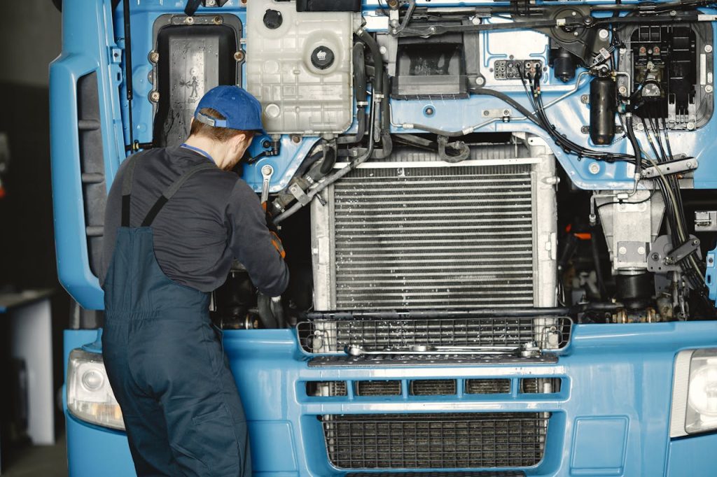 Mechanic in uniform working on a truck engine in an industrial workshop. Perfect for automotive maintenance themes.